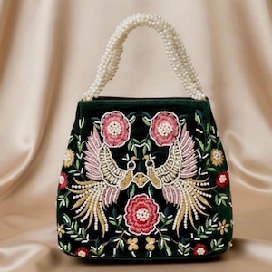 Könnte beinhalten: Dunkelgrüne Samt-Handtasche mit einem gestickten Design mit zwei Pfauen, rosa Blumen und goldenen und weißen Akzenten. Der Griff besteht aus weißen Perlen.