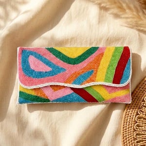 May include: A rectangular clutch bag featuring a vibrant, multi-coloured beaded pattern with wavy, abstract shapes in shades of yellow, green, pink, blue, and red. The flap edge is outlined with white beads, creating a distinct, wavy border.