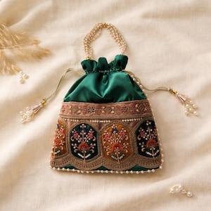 Puede incluir: Un bolso verde de satén con cordón y un panel frontal bordado. El panel presenta diseños florales en rojo, naranja y azul, con detalles dorados y perlas. El bolso tiene un asa de perlas y detalles de borlas.