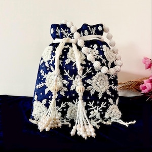Puede incluir: Bolso con cordón azul marino con intrincados abalorios florales blancos. El bolso presenta un cierre de cordón con cuentas y borlas con cuentas. El diseño incluye patrones florales con cuentas blancas y acentos, creando un accesorio decorativo.