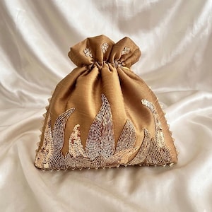 Könnte beinhalten: Ein goldfarbener Beutel mit Kordelzug und aufwendiger floraler Stickerei aus Pailletten und Perlen. Der Beutel hat einen gerafften oberen Teil und einen gewellten Rand, was ihm ein luxuriöses und elegantes Aussehen verleiht. Hergestellt aus glänzendem, satinartigem Material.