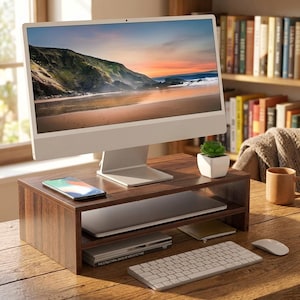 May include: A wooden monitor stand with two shelves holds a computer monitor, laptop, and accessories. A smartphone rests on the top shelf. The monitor displays a scenic beach view. A keyboard and mouse are in the foreground.