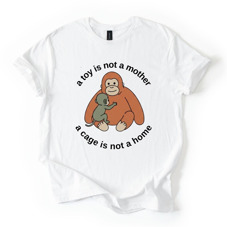May include: White t-shirt featuring a cartoon orangutan and baby orangutan in shades of brown and green. The text "a toy is not a mother, a cage is not a home" is printed around the image in black.