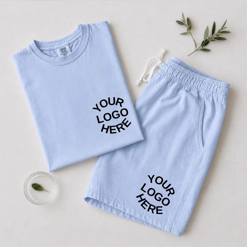 May include: A light blue t-shirt and matching shorts set featuring the black text YOUR LOGO HERE printed on the chest of the shirt and the lower leg of the shorts. The shorts include a white drawstring at the elastic waistband.