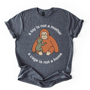 May include: A heather gray t-shirt featuring a cartoon orangutan hugging a baby orangutan. The text "a toy is not a mother, a cage is not a home" is printed in a circular pattern around the image.