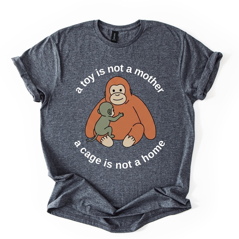 May include: A heather gray t-shirt featuring a cartoon orangutan hugging a baby orangutan. The text "a toy is not a mother, a cage is not a home" is printed in a circular pattern around the image.