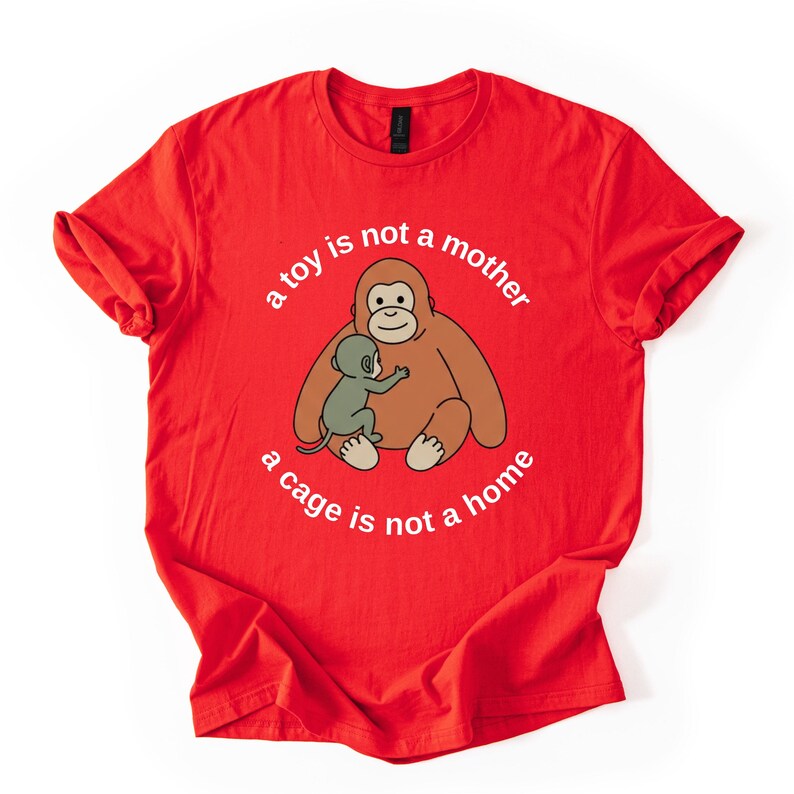 May include: Red t-shirt featuring a cartoon orangutan hugging a smaller ape, with the text "a toy is not a mother, a cage is not a home" in a circular design. The shirt is made of a soft material.