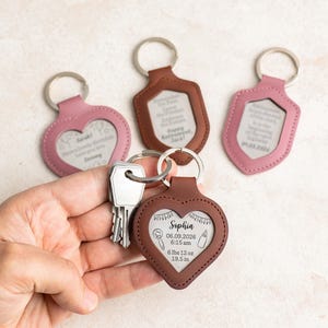 May include: A collection of personalized keychains in various shapes and colors, including pink and brown. One keychain is heart-shaped and engraved with the name "Sophia", date, time, weight, and length. Other keychains have engraved text.