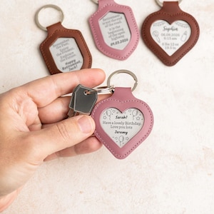 May include: A collection of personalized keychains in various shapes, including a heart and shield. The keychains are made of leather in shades of brown and pink, with silver key rings. Some keychains have engraved text, such as birthday wishes and retirement messages.