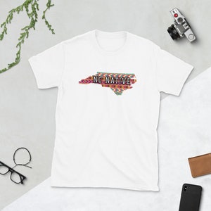 Könnte beinhalten: Weißes T-Shirt mit einem bunten Umriss des Bundesstaates North Carolina und dem Text "NC NATIVE" innerhalb des Umrisses.