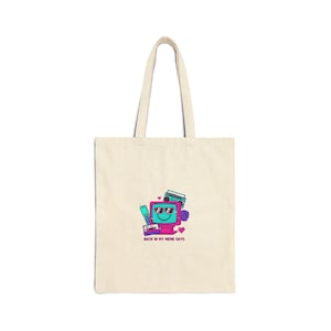 May include: Beige tote bag featuring a retro-themed graphic. The design includes a smiling television with sunglasses, a boombox, a cell phone, and the text "BACK IN MY MEME DAYS" in a retro font. The bag has long handles.