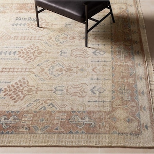 Peut inclure: Tapis de sol beige et marron à motifs avec un motif de bordure. Le tapis présente des motifs géométriques et d'inspiration tribale dans des tons de marron, beige et bleu. Une chaise noire est partiellement visible.