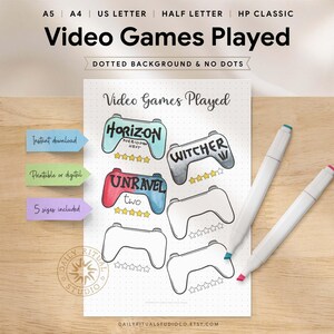 May include: A printable video game tracker with controller illustrations. The sheet includes the text "Video Games Played" and features game titles like "Horizon" and "Unravel." Two white markers with colored tips are on the wooden surface.