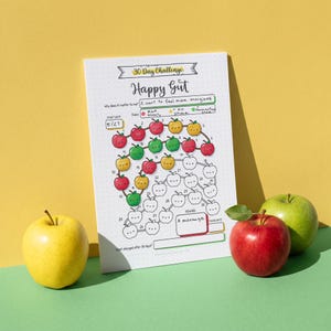 Może przedstawiać: Biały papierowy arkusz do śledzenia 30 Day Challenge Happy Gut z wzorem w kropki. Projekt zawiera ponumerowane ilustracje jabłek, niektóre pokolorowane na czerwono, zielono lub żółto, a inne w formie konturów. Tekst zawiera "30 Day Challenge", "Happy Gut" oraz "A massage".