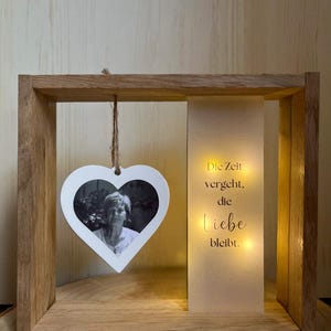 Könnte beinhalten: Holz-Fotorahmen mit herzförmigem Ausschnitt, der ein Schwarz-Weiß-Foto enthält. Der Rahmen hat eine beleuchtete Tafel mit dem deutschen Text "Die Zeit vergeht, die Liebe bleibt."