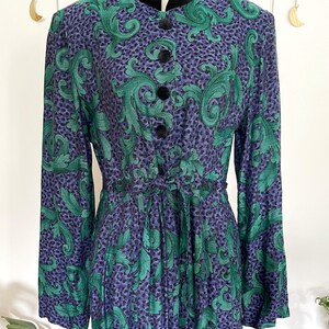 May include: A vintage dress with a high collar and long sleeves. The dress features a pattern of green leaves on a purple background with black dots. It has black velvet trim and buttons, and a matching tie belt.