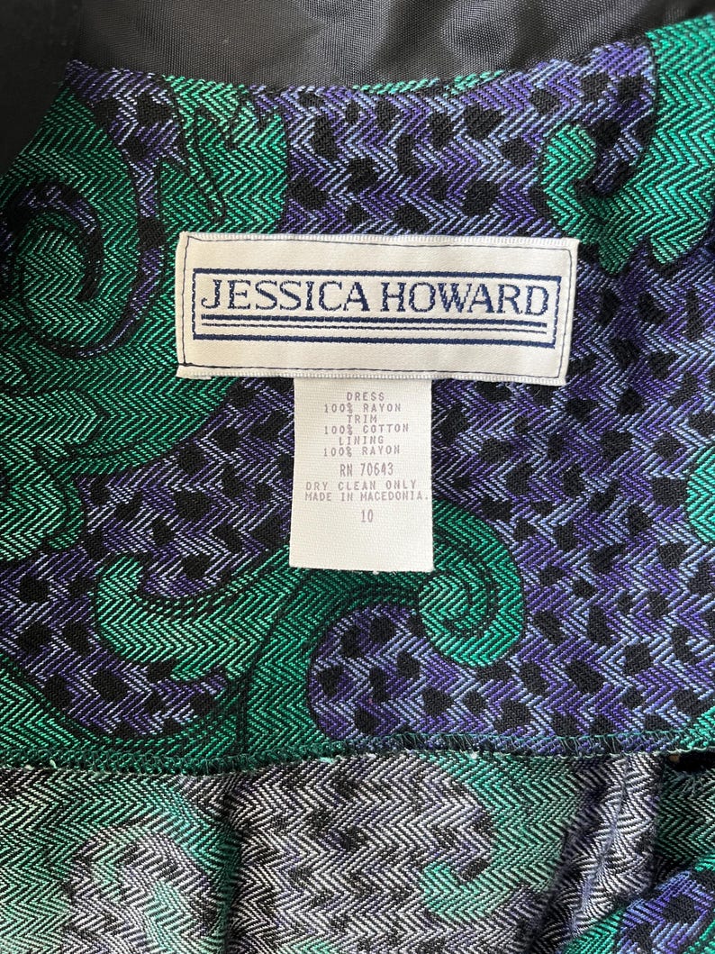 May include: Detail of a dress featuring a green, black, and purple paisley design. The label reads "JESSICA HOWARD" and includes fabric composition and care instructions. The dress is size 10.