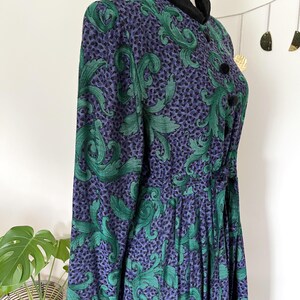 May include: A vintage dress with a high collar and long sleeves. The dress features a pattern of green leaves on a purple background. It has black buttons and a black velvet collar. The dress is displayed on a mannequin.