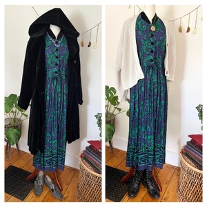 May include: Two outfits showcasing a long, patterned dress with green and purple floral designs. One outfit includes a black hooded coat, the other a cream cardigan. The dress has a button-up front and a tie waist. Accessories include a necklace and shoes.