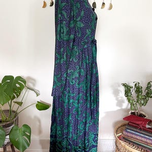 May include: A long, vintage dress with a dark blue and green floral pattern. The dress has a black velvet collar and buttons down the front. The skirt is pleated and reaches the ankles. The dress is displayed on a mannequin.