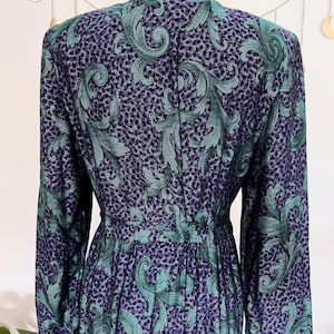May include: A vintage dress with a teal green and purple swirl pattern on a dark background. The dress has long sleeves, a fitted waist, and a black velvet collar. The fabric has a textured appearance.
