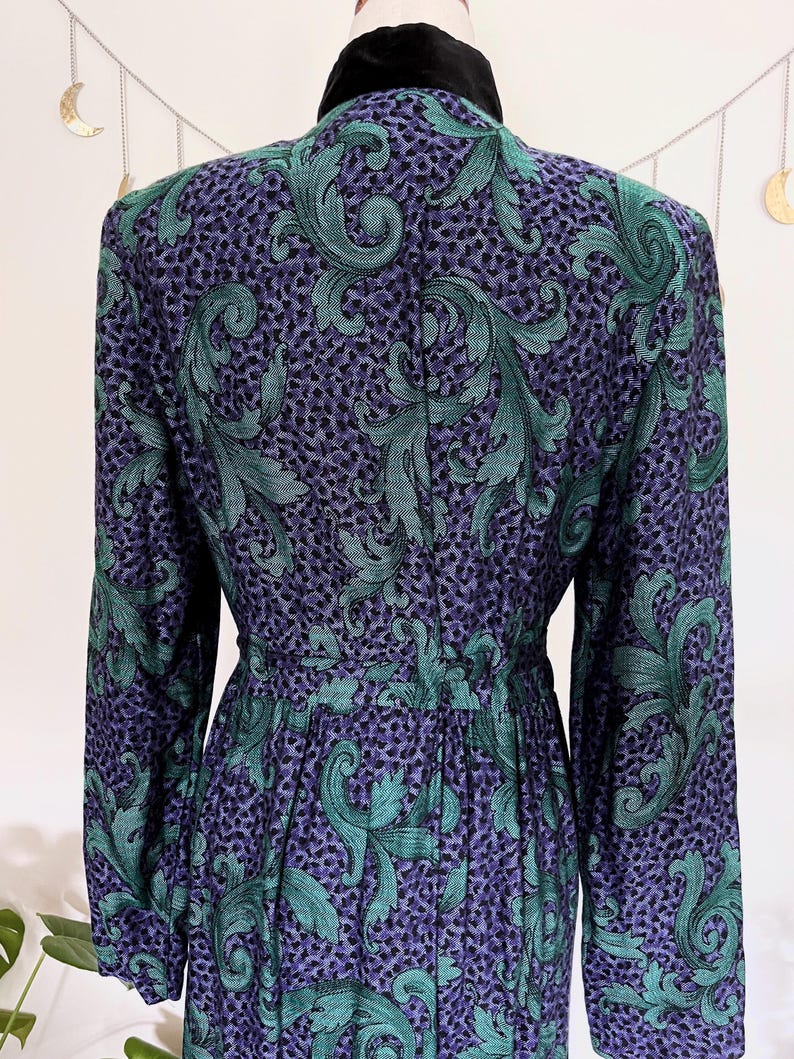 May include: A vintage dress with a teal green and purple swirl pattern on a dark background. The dress has long sleeves, a fitted waist, and a black velvet collar. The fabric has a textured appearance.