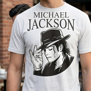 Könnte beinhalten: Ein hellgraues T-Shirt mit einer Schwarz-Weiß-Grafik von Michael Jackson. Die Grafik enthält den Namen "MICHAEL JACKSON" über einer Illustration von Jackson mit Hut und Handschuh.