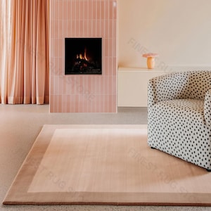Puede incluir: Un salón moderno con una alfombra color rubor con un borde más oscuro, un sillón estampado y una chimenea con un marco de azulejos rosas. Unas cortinas rosas suaves enmarcan una ventana, y las paredes están pintadas en un tono neutro complementario.