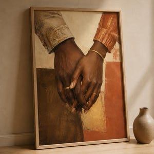 May include: A framed wall art print depicting two dark-skinned hands held together. The hands are adorned with gold rings and a gold bracelet, with sleeves in beige and rust-orange. The background features abstract blocks of brown, cream, and terracotta.