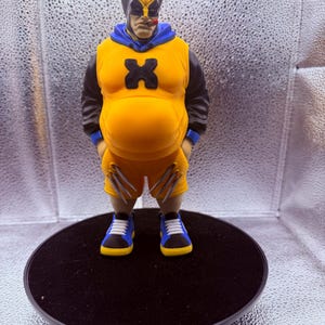 May include: A stylized figurine of a character wearing a yellow and blue hooded sleeveless shirt with a black X emblem, black sleeves, yellow shorts with silver claw accents, and blue and yellow sneakers. The character has a cigar in its mouth.