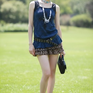 May include: A woman's outfit featuring a blue striped tank top with black straps, a leopard print mini skirt, and a black belt. She is also wearing a necklace and carrying a black purse. The outfit is completed with black flats.