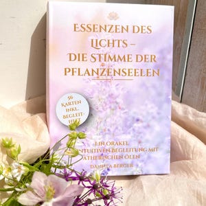 Könnte beinhalten: Eine rechteckige Orakelkarten-Box mit dem Titel Essenzen des Lichts – Die Stimme der Pflanzenseelen von Daniela Berger. Die weiße Box zeigt einen lavendelfarbenen Blumenhintergrund, goldene Schrift und einen runden Aufkleber mit 56 Karten inkl. Begleitheft.
