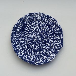 Può includere: Un sottobicchiere rotondo, lavorato all'uncinetto a mano, con un motivo a spirale. Il sottobicchiere è realizzato con filato blu navy e bianco. Il design a trama fitta crea una superficie strutturata. Adatto per l'arredamento della casa.