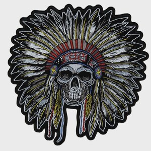 May include: An embroidered patch featuring a human skull wearing a large, detailed feathered headdress. The design uses black, white, grey, red, and yellow thread, with a prominent geometric pattern on the headband and dangling side feathers.