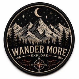 May include: A circular embroidered patch featuring a black background with a white mountain range, pine trees, a crescent moon, and stars. The text WANDER MORE and EXPLORE is stitched in white, accompanied by a compass rose and arrow graphic.