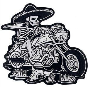 May include: An embroidered patch featuring a skeleton wearing a sombrero and a cape while riding a motorcycle. Below the motorcycle, a steer skull rests on the ground. The design is rendered in black and white thread with a thick black border.