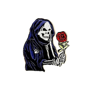 Op de afbeelding: Een geborduurde patch met een afbeelding van een magere Hein-figuur in een donkerblauwe kapmantel. De figuur heeft een wit schedelgezicht en houdt een enkele rode roos met een groene steel en bladeren vast in de skeletachtige hand.