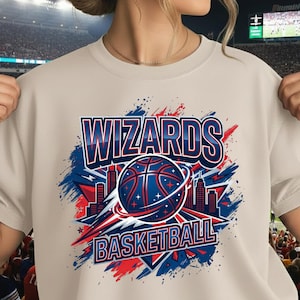 Könnte beinhalten: Beiges Rundhals-Sweatshirt mit einem grafischen Design mit dem Text "WIZARDS BASKETBALL". Das Design umfasst einen Basketball, eine Skyline und Farbspritzer in Rot, Weiß und Blau.