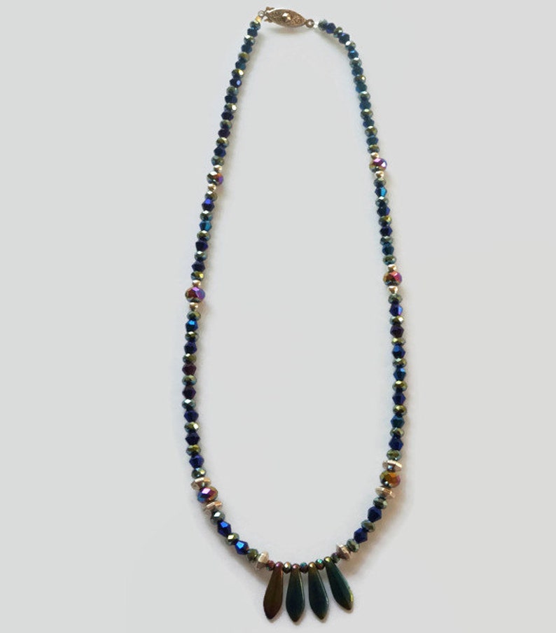 May include: A blue and iridescent crystal beaded necklace with a gold clasp and a pendant of three dark green iridescent teardrop-shaped stones.