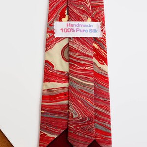 May include: A red and cream silk tie with a marbled pattern. The tie has a burgundy lining and a label that reads "Handmade 100% Pure Silk".
