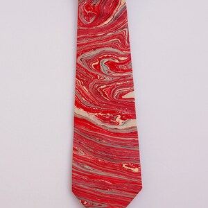 May include: A red and cream tie with a marbled pattern. The tie is made of silk and has a pointed tip.