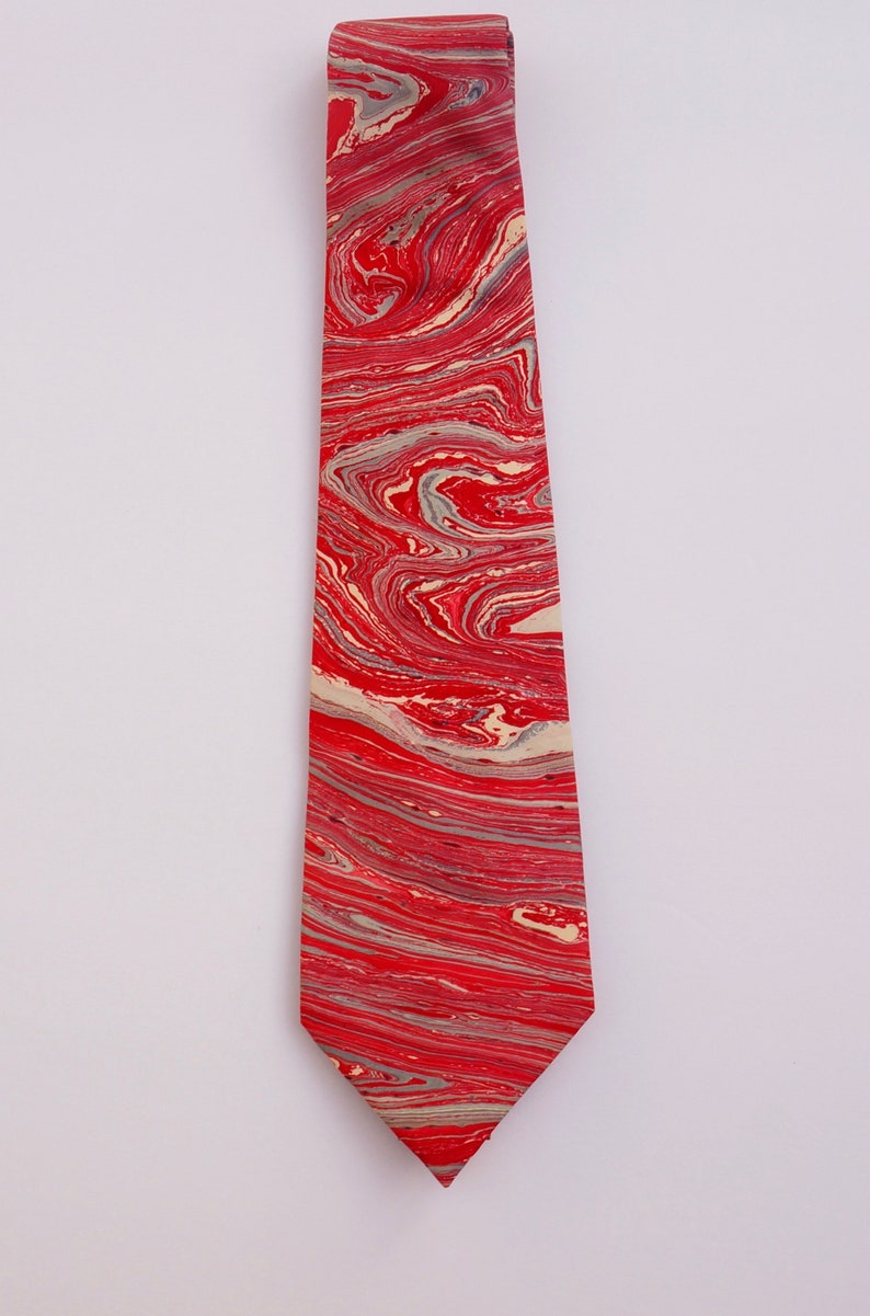 May include: A red and cream tie with a marbled pattern. The tie is made of silk and has a pointed tip.