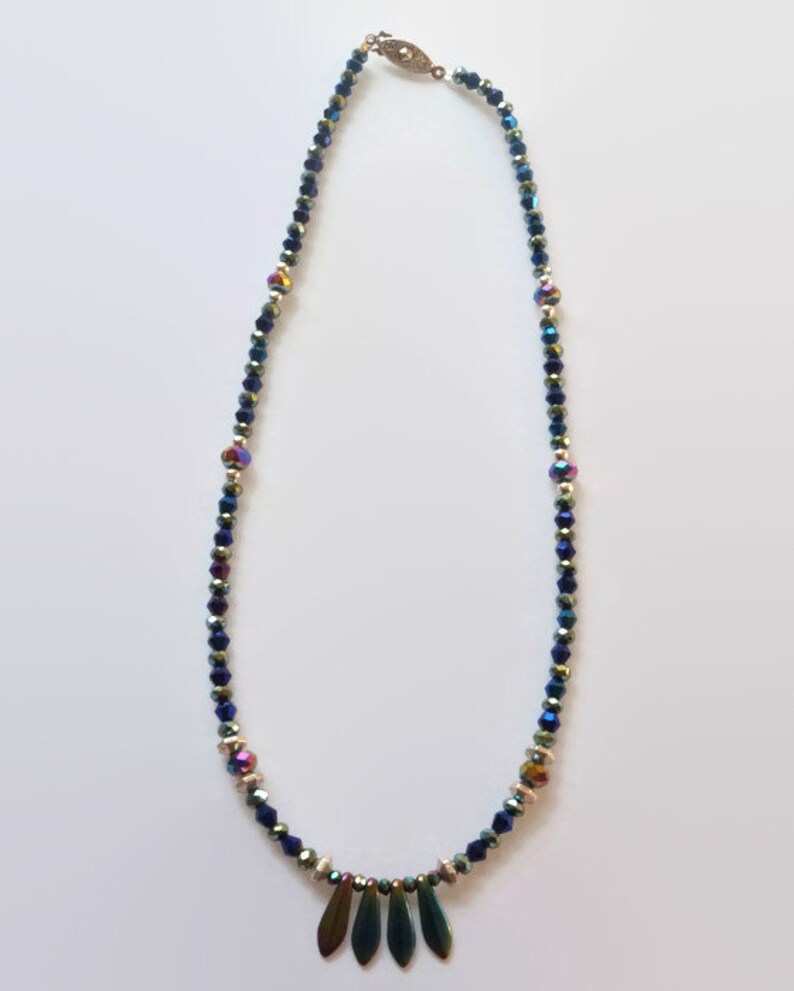 May include: A blue iridescent crystal necklace with a gold clasp and a pendant of four iridescent metal leaves.