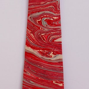 May include: A red and cream tie with a marbled pattern. The tie is made of a smooth fabric and has a pointed tip.