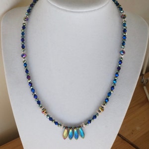 May include: A blue iridescent crystal necklace with a silver and gold accent. The necklace has a pendant with four iridescent blue teardrop-shaped crystals.