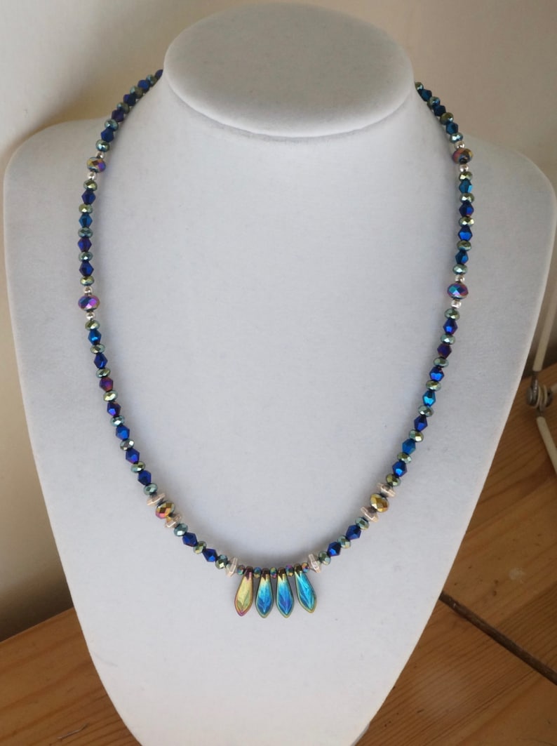 May include: A blue iridescent crystal necklace with a silver and gold accent. The necklace has a pendant with four iridescent blue teardrop-shaped crystals.