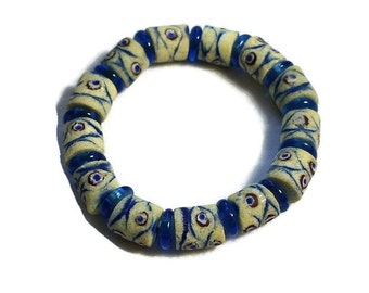 May include: A white and blue beaded bracelet with a repeating pattern of blue eyes. The beads are made of glass and are strung on a clear elastic cord.