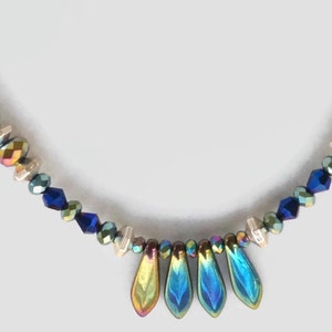 May include: A necklace with iridescent blue, green, and gold beads, with a teardrop-shaped pendant made of iridescent blue and green glass.