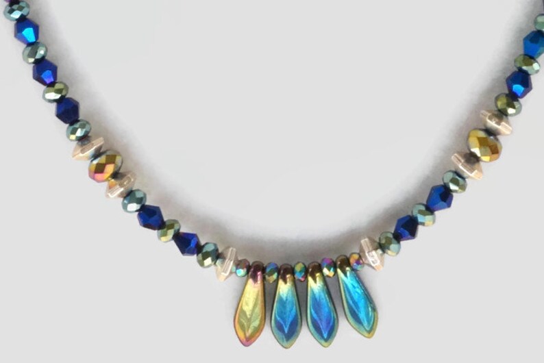 May include: A necklace with iridescent blue, green, and gold beads, with a teardrop-shaped pendant made of iridescent blue and green glass.