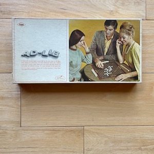 May include: A vintage box game called "AD-LIB" with a colorful illustration of three people playing the game. The box features a description of the game, which is a word game that involves creating sentences and stories.